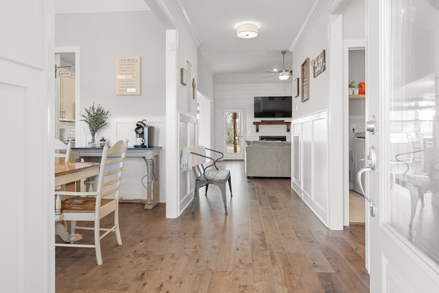 hall featuring wood finished floors, ornamental molding, and a decorative wall