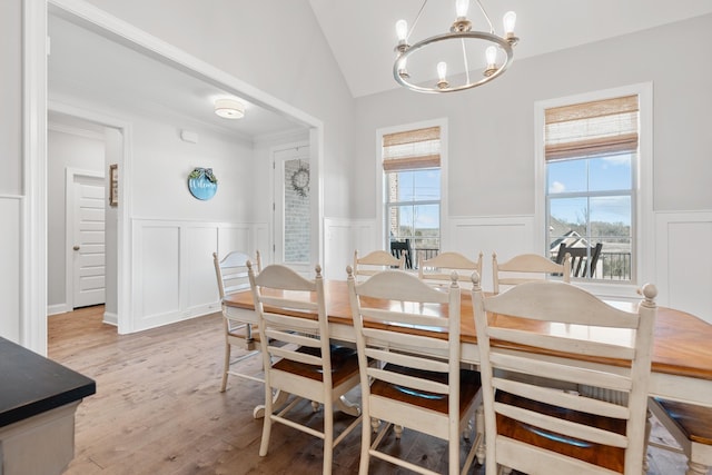 dining area featuring a wainscoted wall, light wood-type flooring, vaulted ceiling, a notable chandelier, and a decorative wall