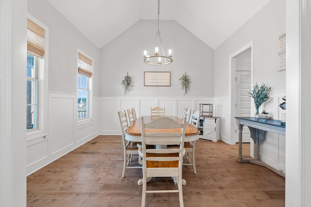 dining area featuring a chandelier, vaulted ceiling, wood finished floors, and wainscoting