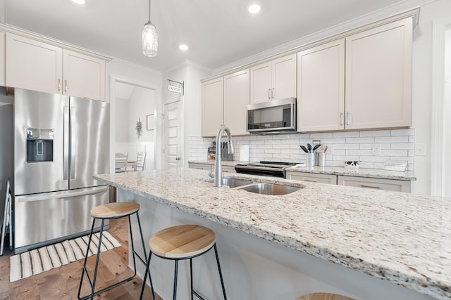 kitchen featuring stainless steel appliances, a breakfast bar area, a sink, light stone counters, and ornamental molding
