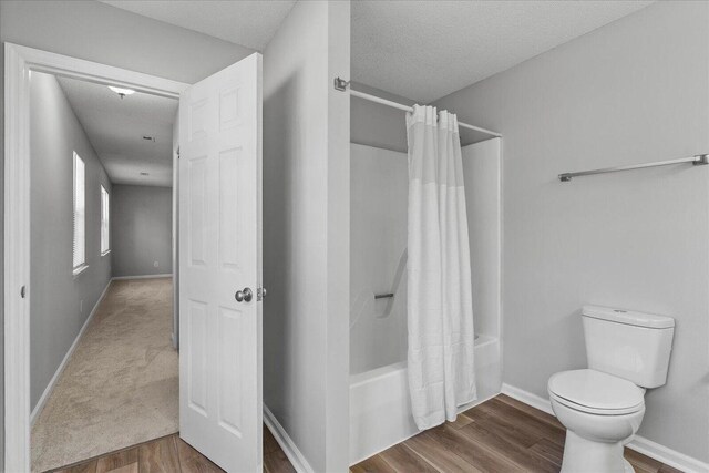 bathroom featuring toilet, wood finished floors, baseboards, shower / tub combo with curtain, and a textured ceiling