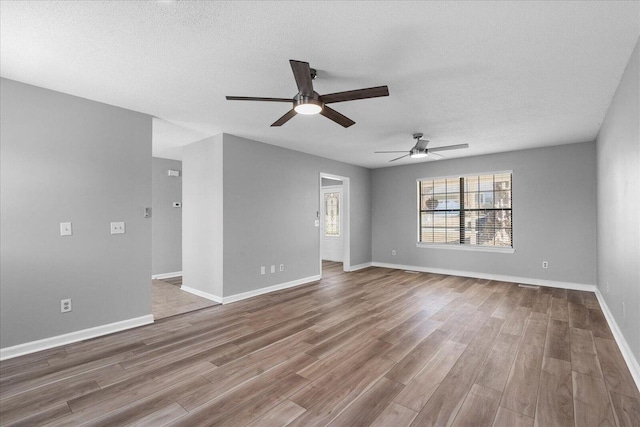 unfurnished room featuring ceiling fan, wood finished floors, a textured ceiling, and baseboards