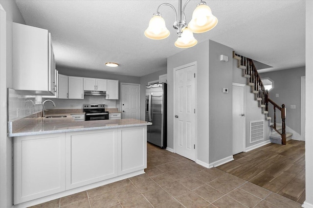 kitchen with appliances with stainless steel finishes, a sink, under cabinet range hood, a chandelier, and a peninsula