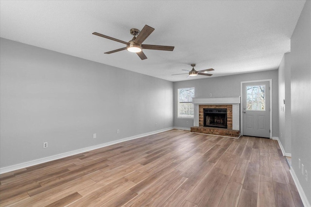 unfurnished living room featuring ceiling fan, light wood-type flooring, baseboards, and a brick fireplace