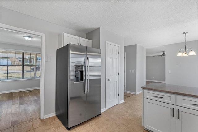 kitchen with stainless steel fridge with ice dispenser, a textured ceiling, a chandelier, baseboards, and white cabinetry