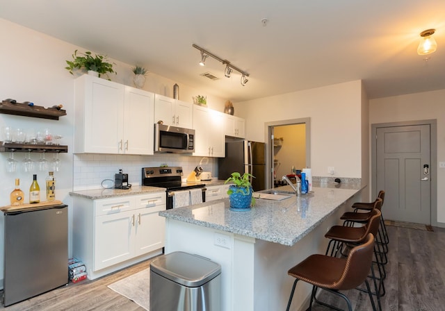 782 Riverfront Pkwy Unit 301, Chattanooga, TN 37402 - kitchen with stainless steel appliances, a peninsula, light wood-type flooring, white cabinetry, and a breakfast bar