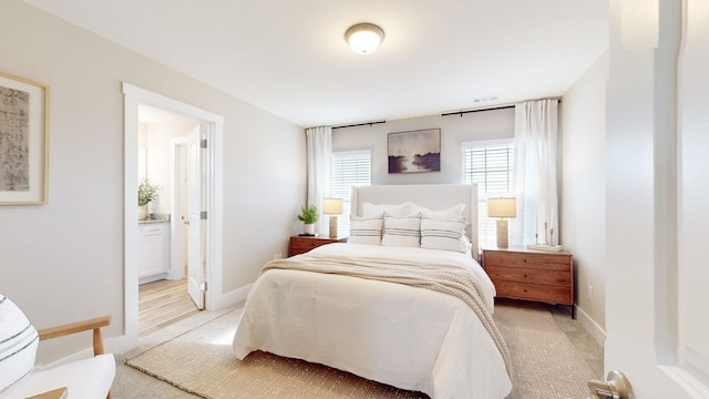 bedroom with ensuite bathroom, light colored carpet, and baseboards