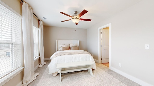 bedroom featuring light carpet, a ceiling fan, baseboards, and multiple windows