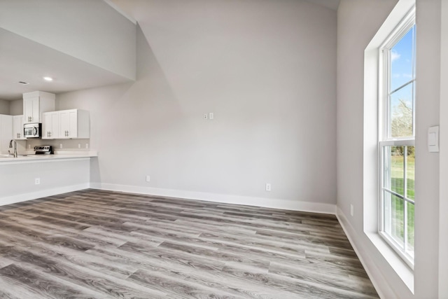 unfurnished living room featuring recessed lighting, wood finished floors, baseboards, and a sink
