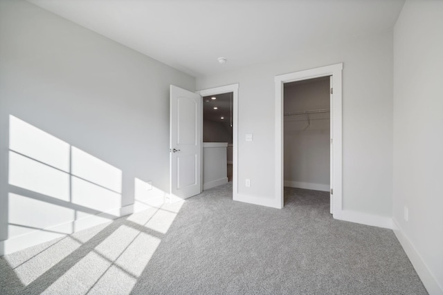unfurnished bedroom with a spacious closet, baseboards, carpet, and a closet