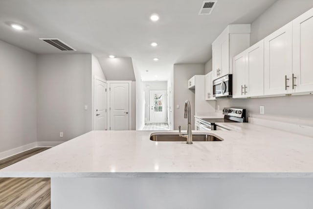 kitchen featuring light stone counters, wood finished floors, a sink, appliances with stainless steel finishes, and visible vents