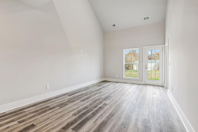 spare room with baseboards, wood finished floors, visible vents, and high vaulted ceiling