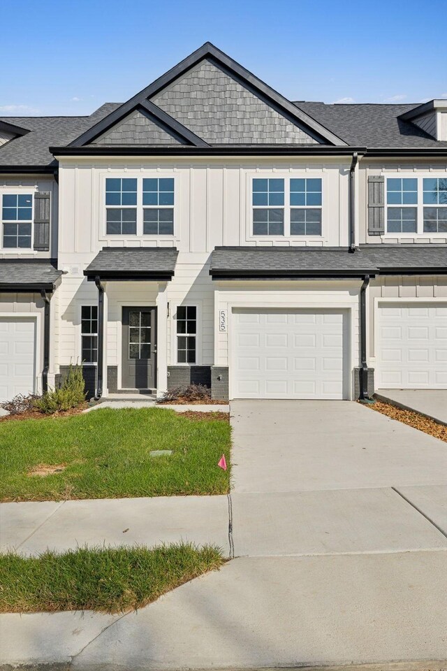 view of property with an attached garage, driveway, board and batten siding, and a front yard