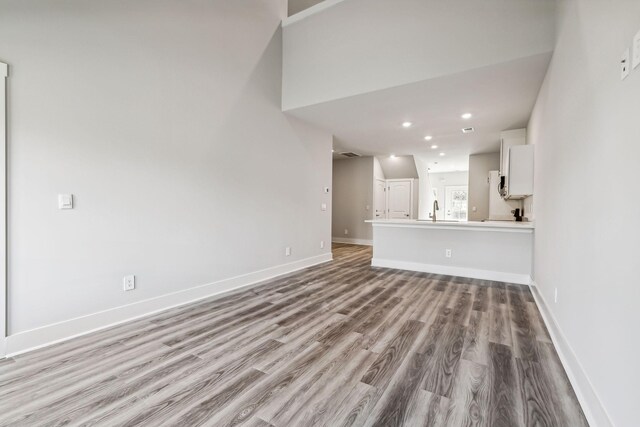 unfurnished living room featuring recessed lighting, wood finished floors, visible vents, a sink, and baseboards