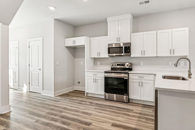 kitchen with stainless steel appliances, light countertops, a sink, light wood-style flooring, and white cabinetry