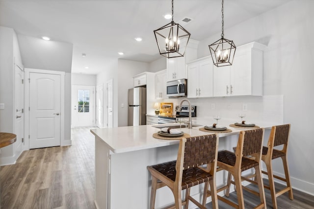 kitchen featuring stainless steel appliances, a breakfast bar, light countertops, visible vents, and white cabinetry