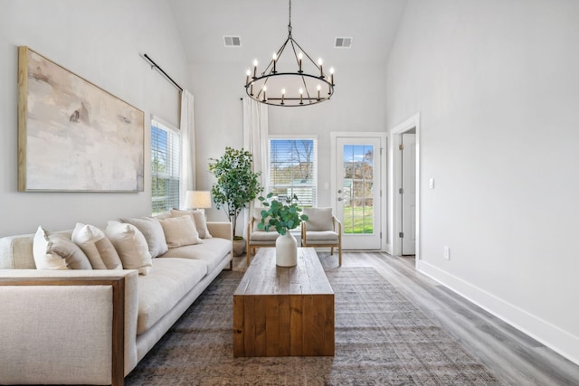 living area with an inviting chandelier, wood finished floors, visible vents, baseboards, and high vaulted ceiling