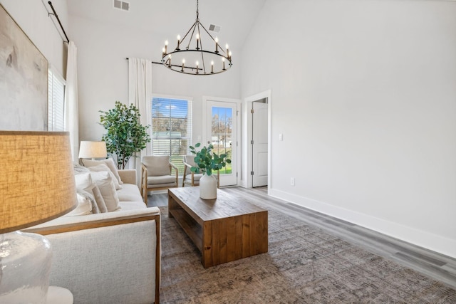 living area featuring wood finished floors, a healthy amount of sunlight, high vaulted ceiling, and an inviting chandelier