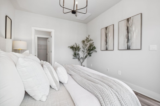 bedroom featuring wood finished floors, a closet, a walk in closet, a chandelier, and baseboards