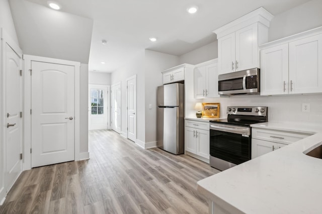kitchen with white cabinets, light wood-type flooring, appliances with stainless steel finishes, and tasteful backsplash