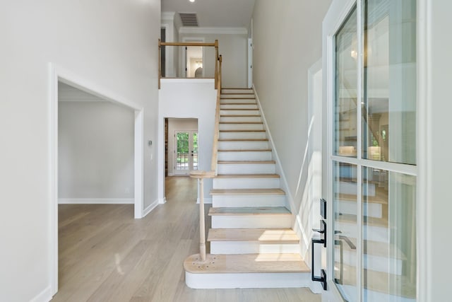 stairs featuring a high ceiling, baseboards, wood finished floors, visible vents, and ornamental molding