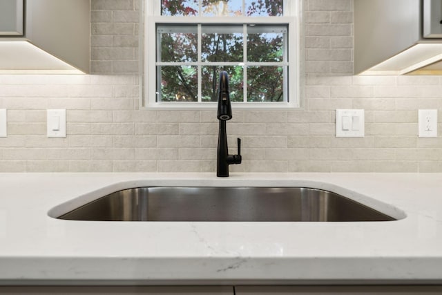 interior details featuring a sink, light stone counters, and decorative backsplash