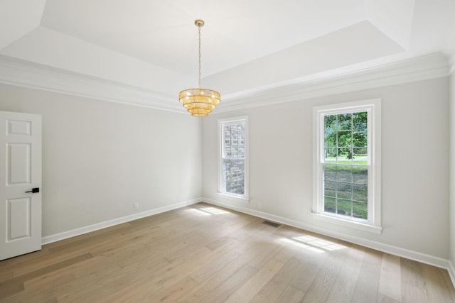 empty room with a raised ceiling, light wood finished floors, a chandelier, and a wealth of natural light