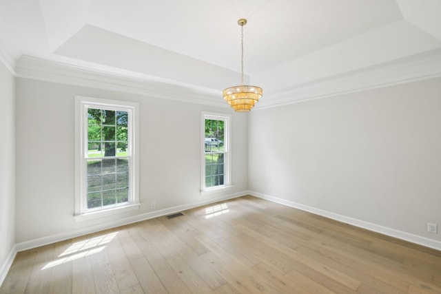spare room featuring baseboards, light wood finished floors, a raised ceiling, and visible vents