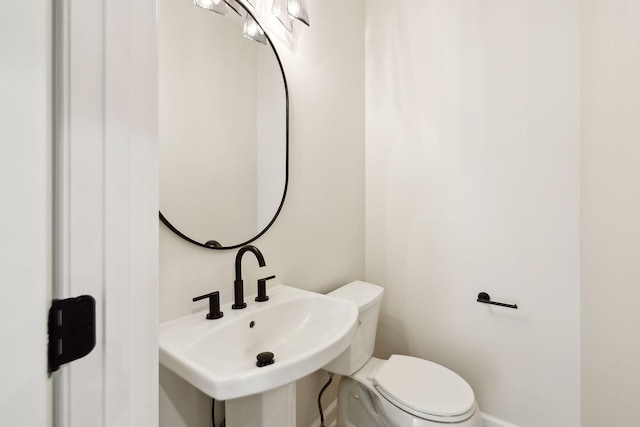 half bath with baseboards, a sink, and toilet