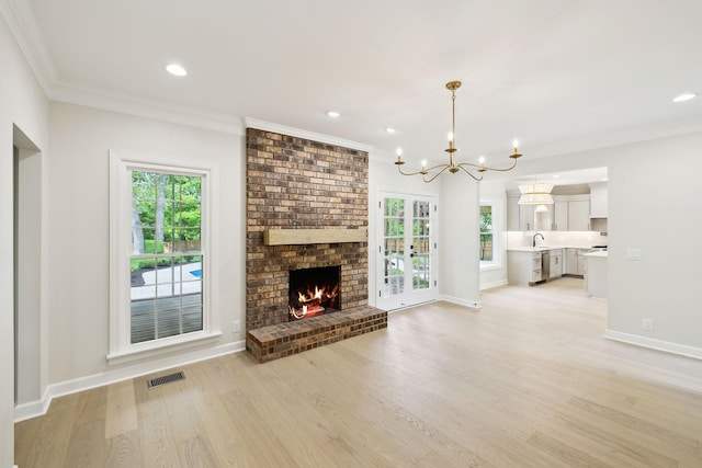 unfurnished living room featuring a fireplace, an inviting chandelier, plenty of natural light, and light wood-style floors