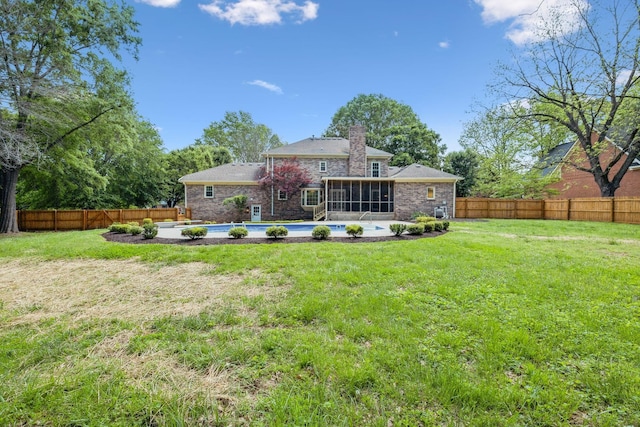 rear view of house featuring stone siding, a sunroom, a fenced backyard, a chimney, and a yard