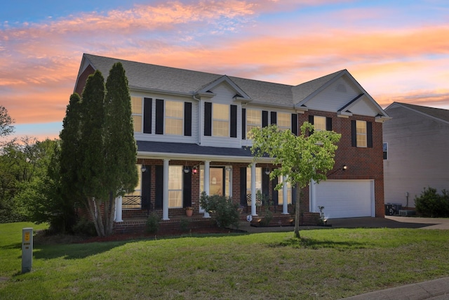 view of front of house featuring a yard, driveway, covered porch, brick siding, and a garage