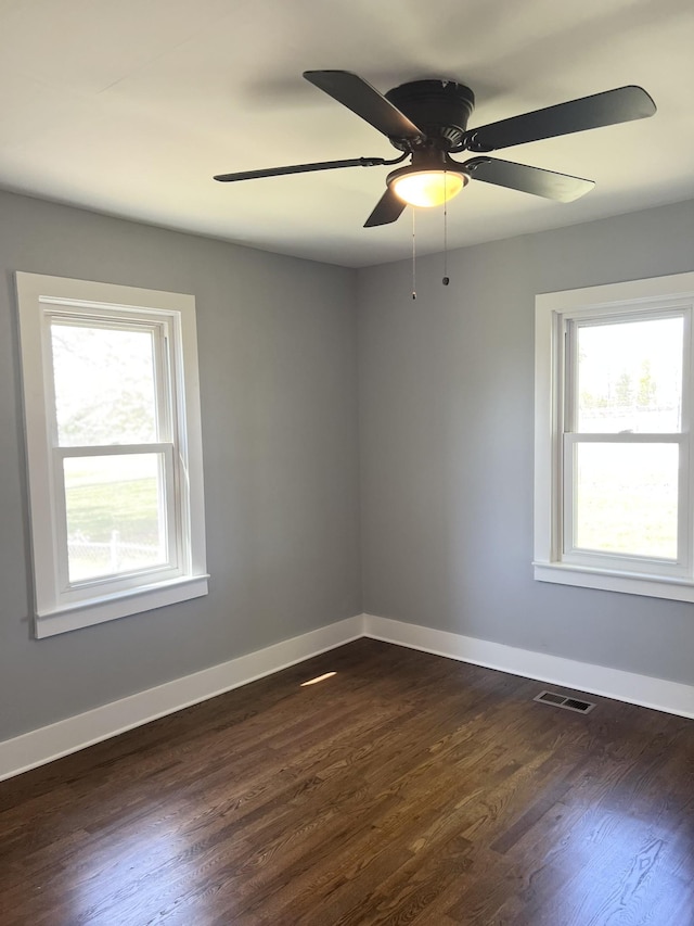empty room featuring plenty of natural light, visible vents, and dark wood finished floors