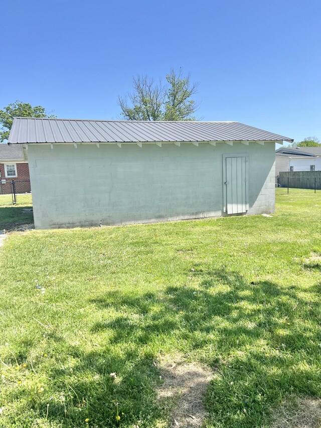 view of home's exterior with fence, a lawn, an outbuilding, and concrete block siding