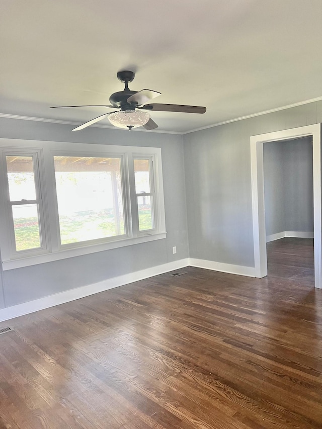 empty room with dark wood finished floors, baseboards, visible vents, a ceiling fan, and crown molding
