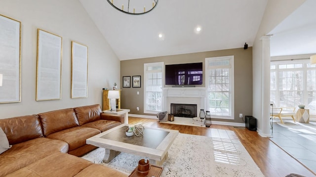 living room featuring a fireplace with flush hearth, recessed lighting, light wood finished floors, baseboards, and high vaulted ceiling