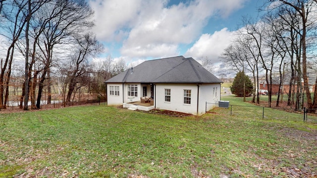 rear view of property featuring roof with shingles, central air condition unit, fence, a yard, and stucco siding
