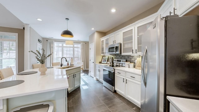 kitchen featuring white cabinets, stainless steel appliances, a sink, decorative light fixtures, and tasteful backsplash
