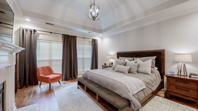 bedroom featuring wood finished floors, a high end fireplace, a chandelier, ornamental molding, and visible vents