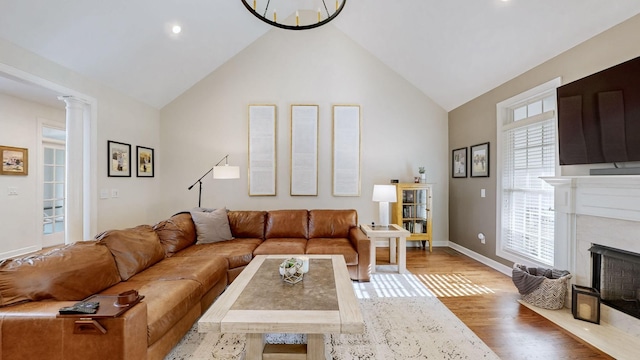 living area with high vaulted ceiling, a high end fireplace, baseboards, and wood finished floors