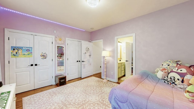 bedroom featuring two closets, wood finished floors, and ensuite bathroom