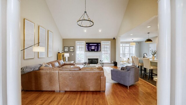 living area featuring recessed lighting, a glass covered fireplace, light wood finished floors, and high vaulted ceiling