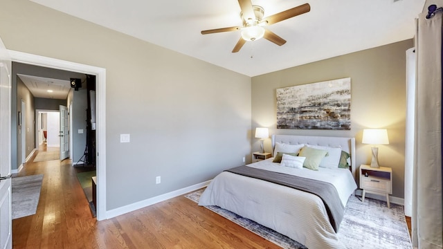 bedroom featuring attic access, baseboards, wood finished floors, and ceiling fan
