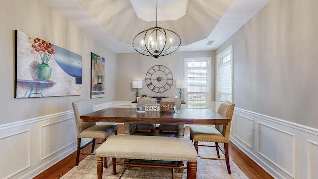 dining space featuring a decorative wall, a wainscoted wall, wood finished floors, and an inviting chandelier
