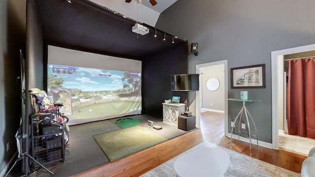 home theater with a towering ceiling, wood finished floors, rail lighting, a ceiling fan, and baseboards