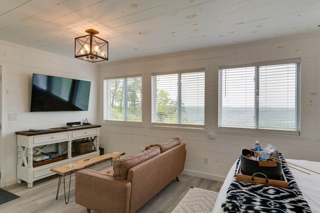 living area with baseboards, ornamental molding, a chandelier, and light wood finished floors