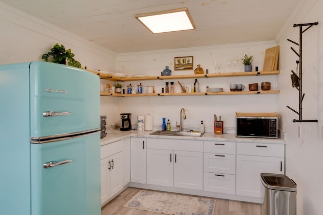 kitchen featuring white cabinets, ornamental molding, a sink, freestanding refrigerator, and light wood-style flooring