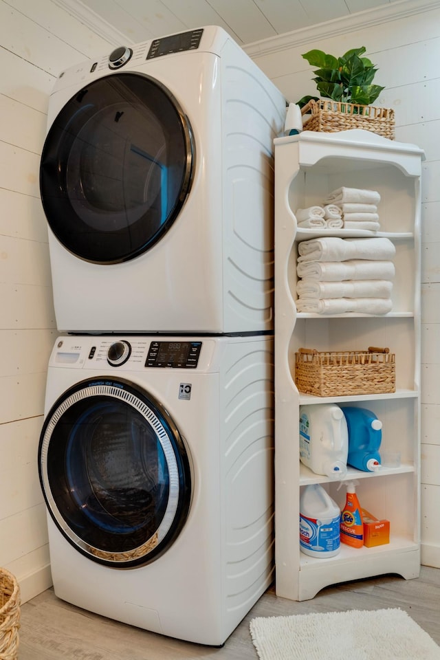 washroom with stacked washer / drying machine, wooden walls, wood finished floors, and laundry area