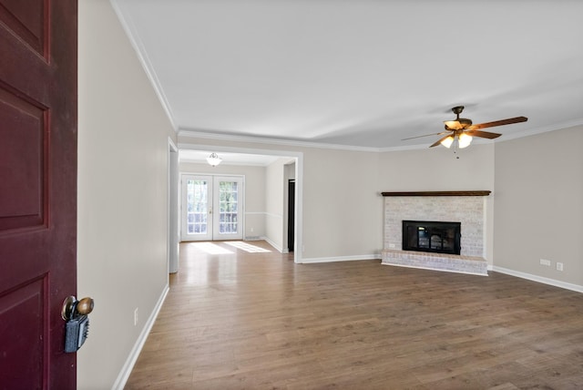 unfurnished living room with baseboards, a ceiling fan, wood finished floors, a fireplace, and ornamental molding