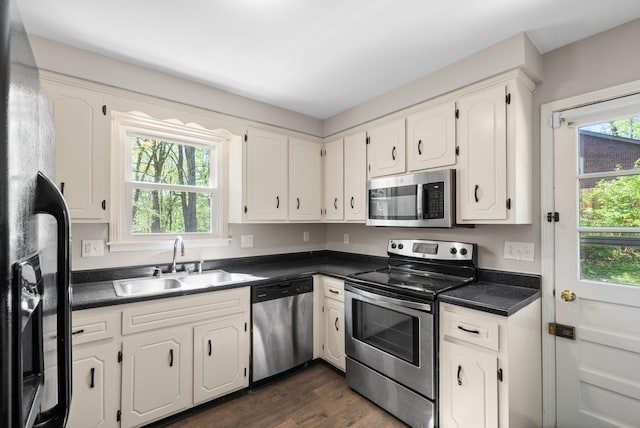 kitchen with dark countertops, a sink, appliances with stainless steel finishes, and dark wood finished floors